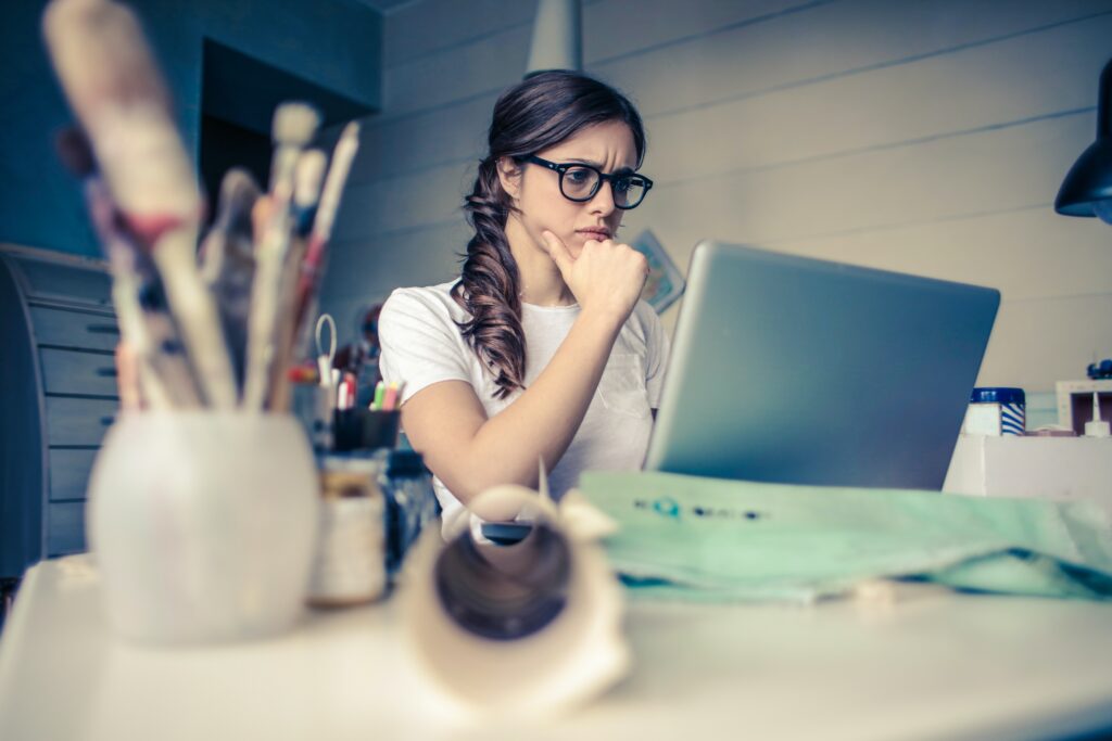 young woman sitting at work desk in front of lap top thinking - Determine Your Investment Goals